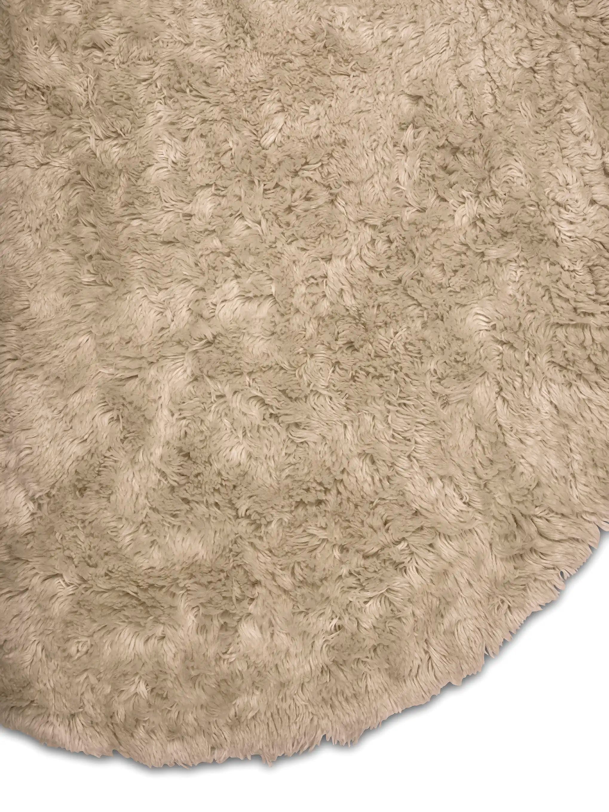 Detaljbild av rund ullmatta Cloudy i beige rya som visar luggens struktur och mattans runda form