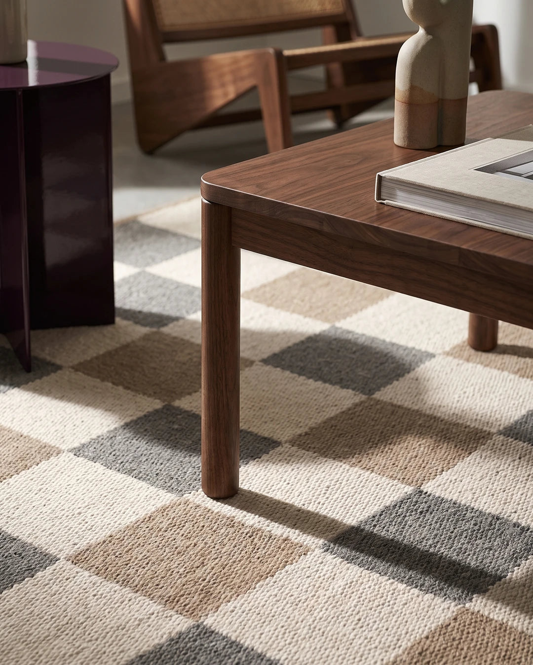 Närbild av handvävd ullmatta Check Grå/Natur från Classic Collection med rutmönster i grå, beige och naturvita toner, under ett mörkt träsoffbord intill ett mörkt vinrött sidobord.