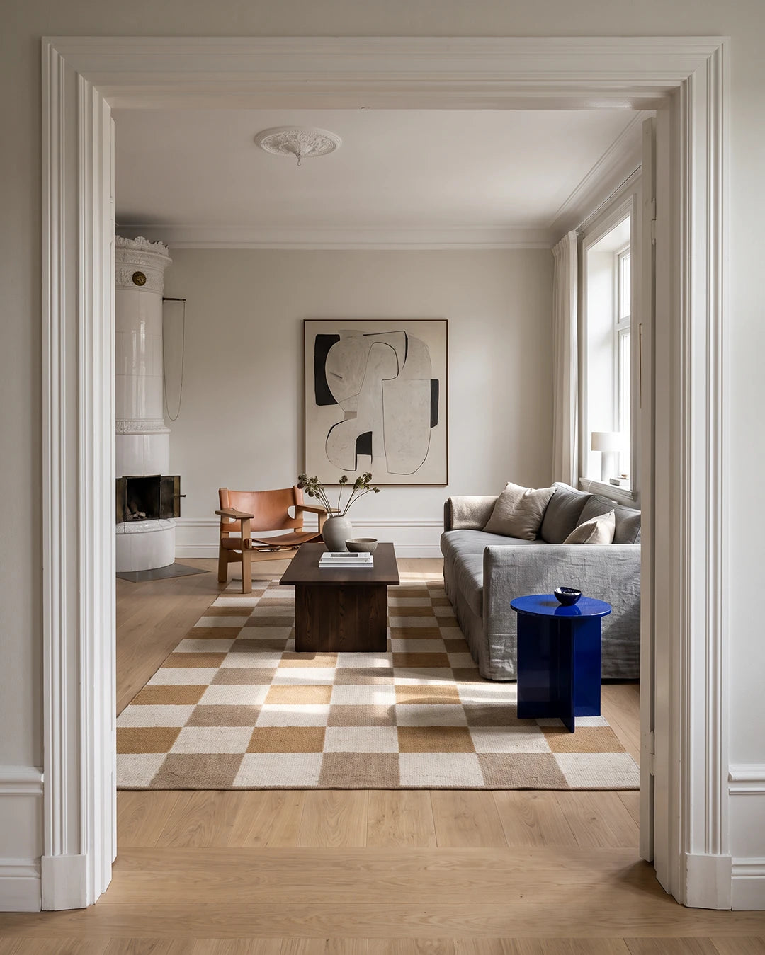 Handvävd ullmatta Check Gul/Natur från Classic Collection med rutmönster i gult, beige och naturvitt, placerad i ett ljust vardagsrum med träsoffbord, grå soffa och fåtölj i trä.