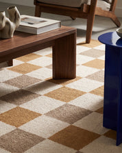 Närbild av handvävd ullmatta Check Gul/Natur från Classic Collection med grafiskt rutmönster i gult, beige och naturvitt, tillsammans med mörkt träbord och blått sidobord.