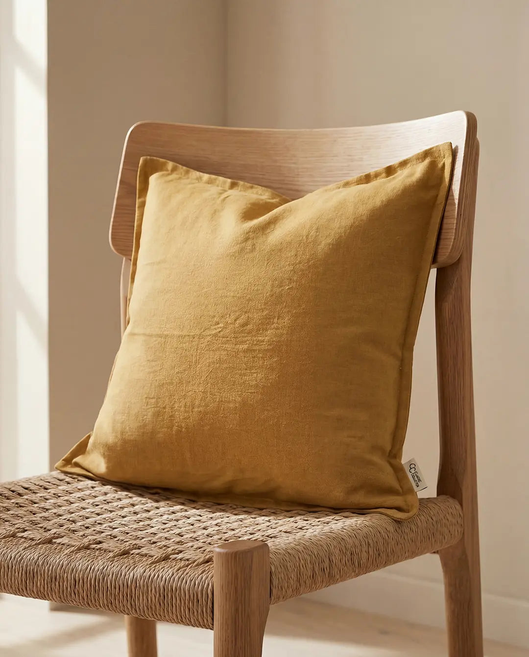 Mustard yellow square linen throw pillow resting on a wooden chair with a woven seat.