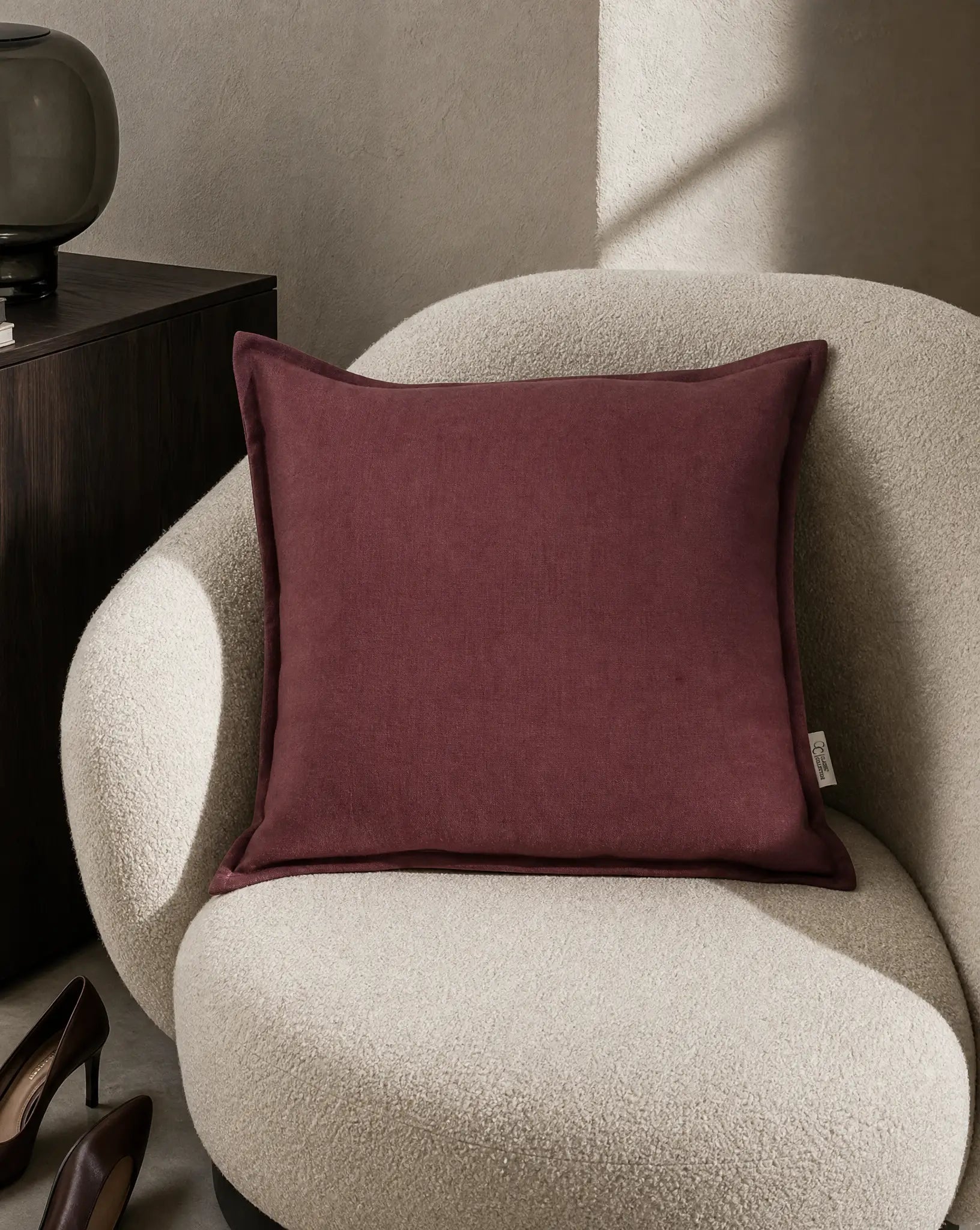 Kuddfodral Classic Linen Burgundy 50x50 cm från Classic Collection i enfärgat linne, stylat i en ljusbeige fåtölj i en varm, neutral interiör.