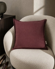Kuddfodral Classic Linen Burgundy 50x50 cm från Classic Collection i enfärgat linne, stylat i en ljusbeige fåtölj i en varm, neutral interiör.