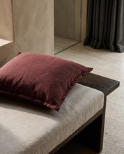 Kuddfodral Classic Linen Burgundy 50x50 cm från Classic Collection enfärgad i linne-bomullblandning. Stylat på en beige dagbädd i en varm, elegant interiör.