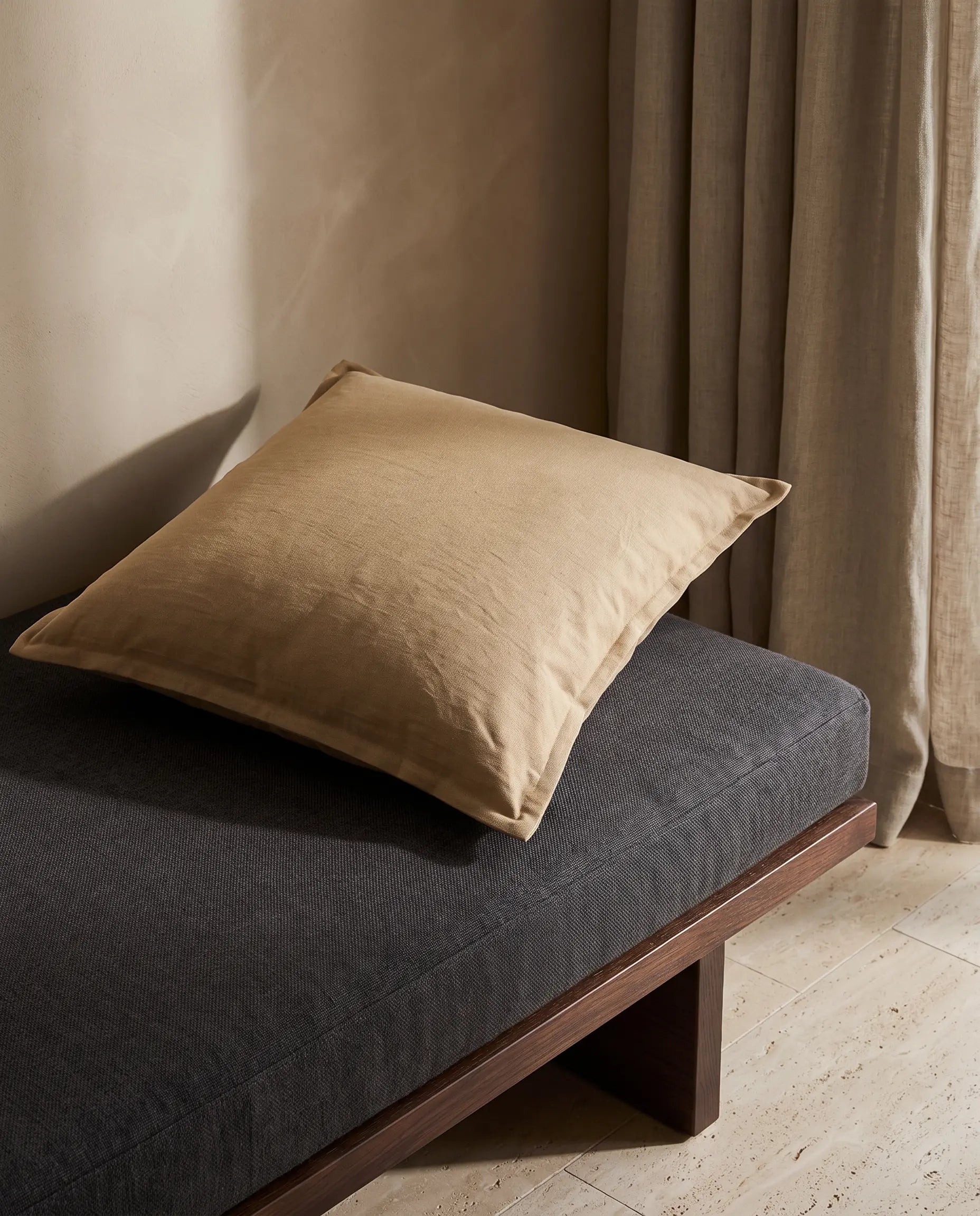 Kuddfodral Classic Linen Mocca 50x50 cm från Classic Collection i enfärgat linne, stylat på enmörkgrå dagbädd i en varm, neutral interiör.