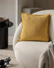 Kuddfodral Classic Linen Ockra 50x50 cm från Classic Collection i enfärgat linne, stylat i en ljus fåtölj i en varm, neutral interiör.