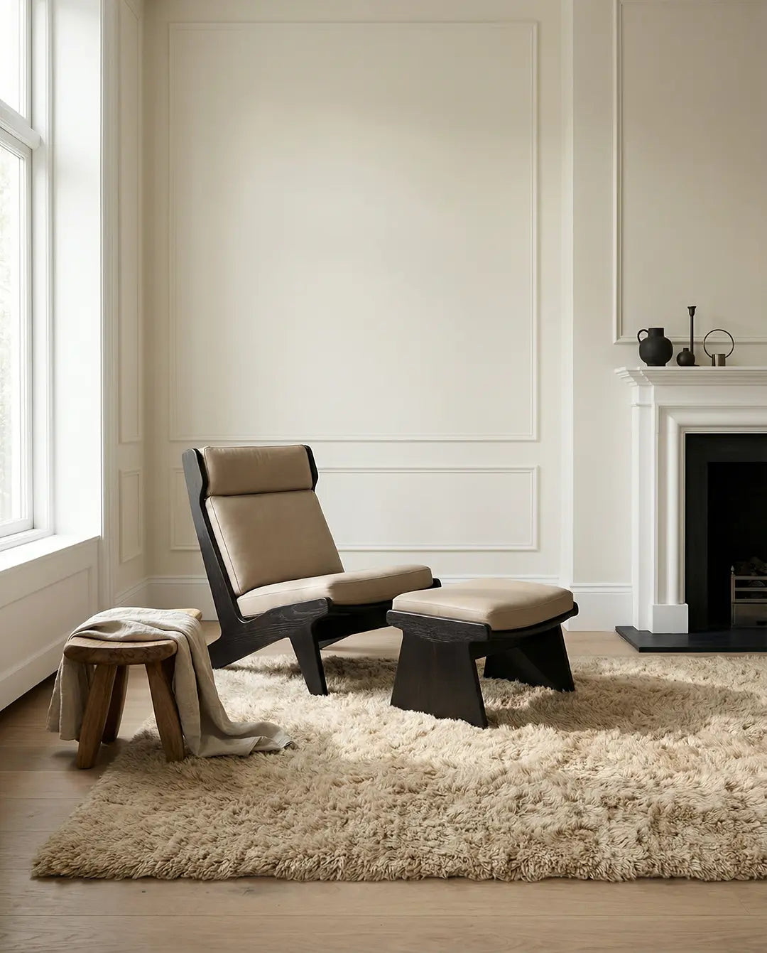 Modern fåtölj med fotpall i mörkt trä och beige läderklädsel, placerad i ett stilrent vardagsrum.