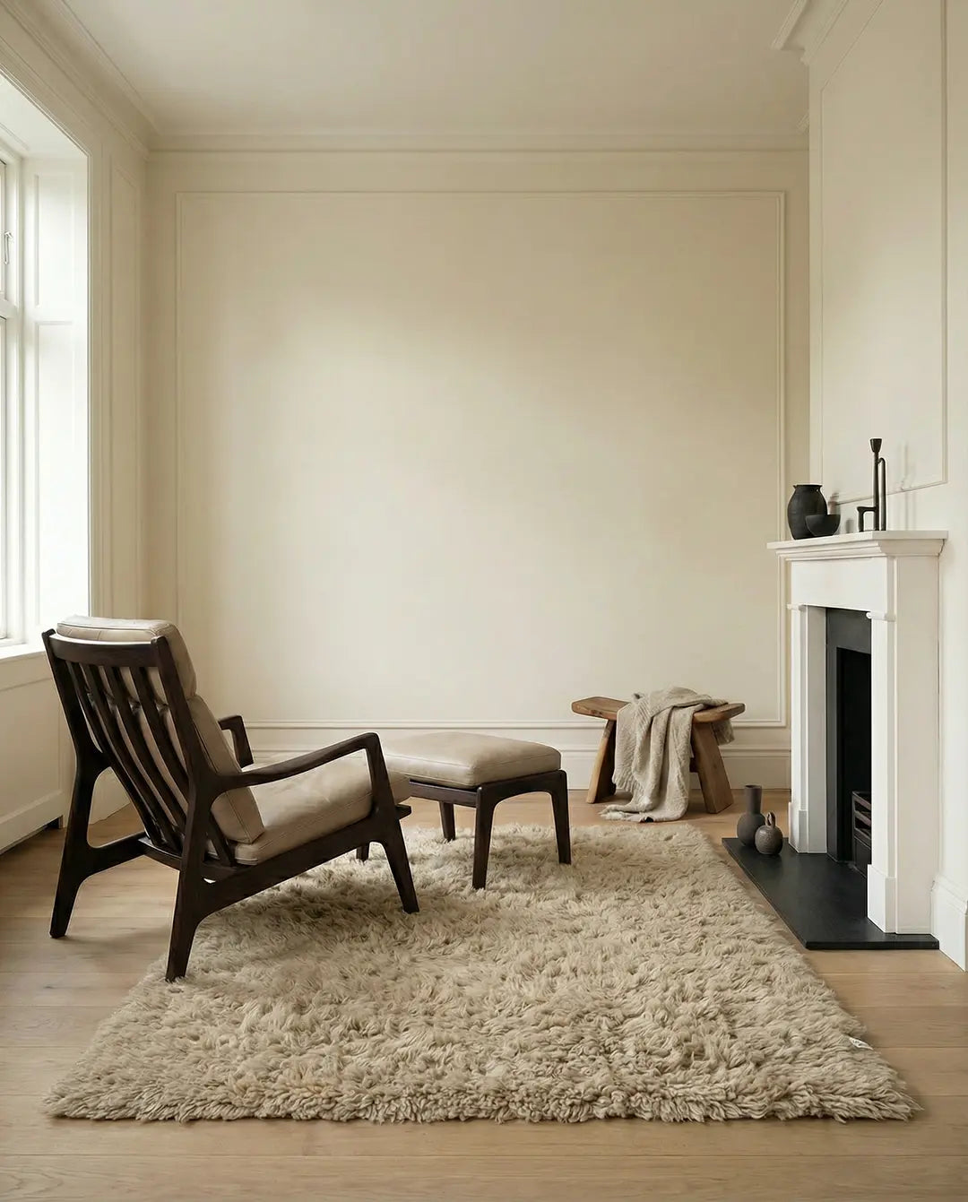 Moderner Lounge-Sessel mit Fußhocker aus dunklem Holz und beigem Lederpolster in einem hellen Wohnzimmer mit Kamin.