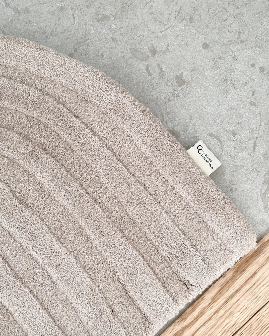 Handgjord dörrmatta Arch i färgen Beige, tillverkad i ull. Närbild som visar den mjukt rundade formen, den strukturerade ytan med diskret bågmönster samt etikett med Classic Collection-logotyp.