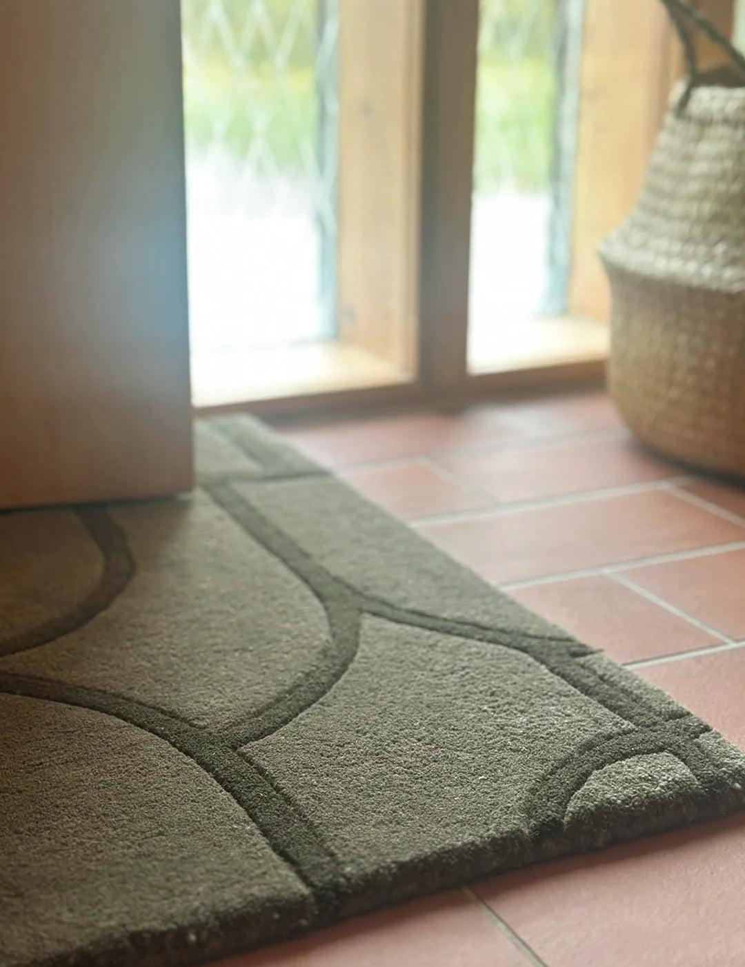 Dörrmatta Modern Abstract Grön i ull placerad vid ytterdörr på terrakottaklinker, med ljusinsläpp från fönster i bakgrunden.