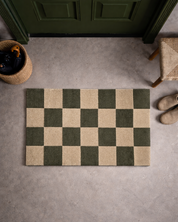 Dörrmatta Square i grön och naturfärgad ull med rutmönster, placerad innanför ytterdörr i hallmiljö