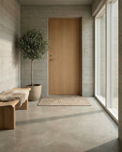 Beiger Eingangs-Teppich mit wellenförmigem Reliefmuster in einem modern eingerichteten Flur mit Holztür und Betonwänden.