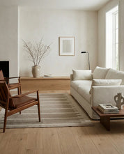 Vardagsrum med beige soffa, mörka träfåtöljer och en randig matta i minimalistisk, skandinavisk stil.