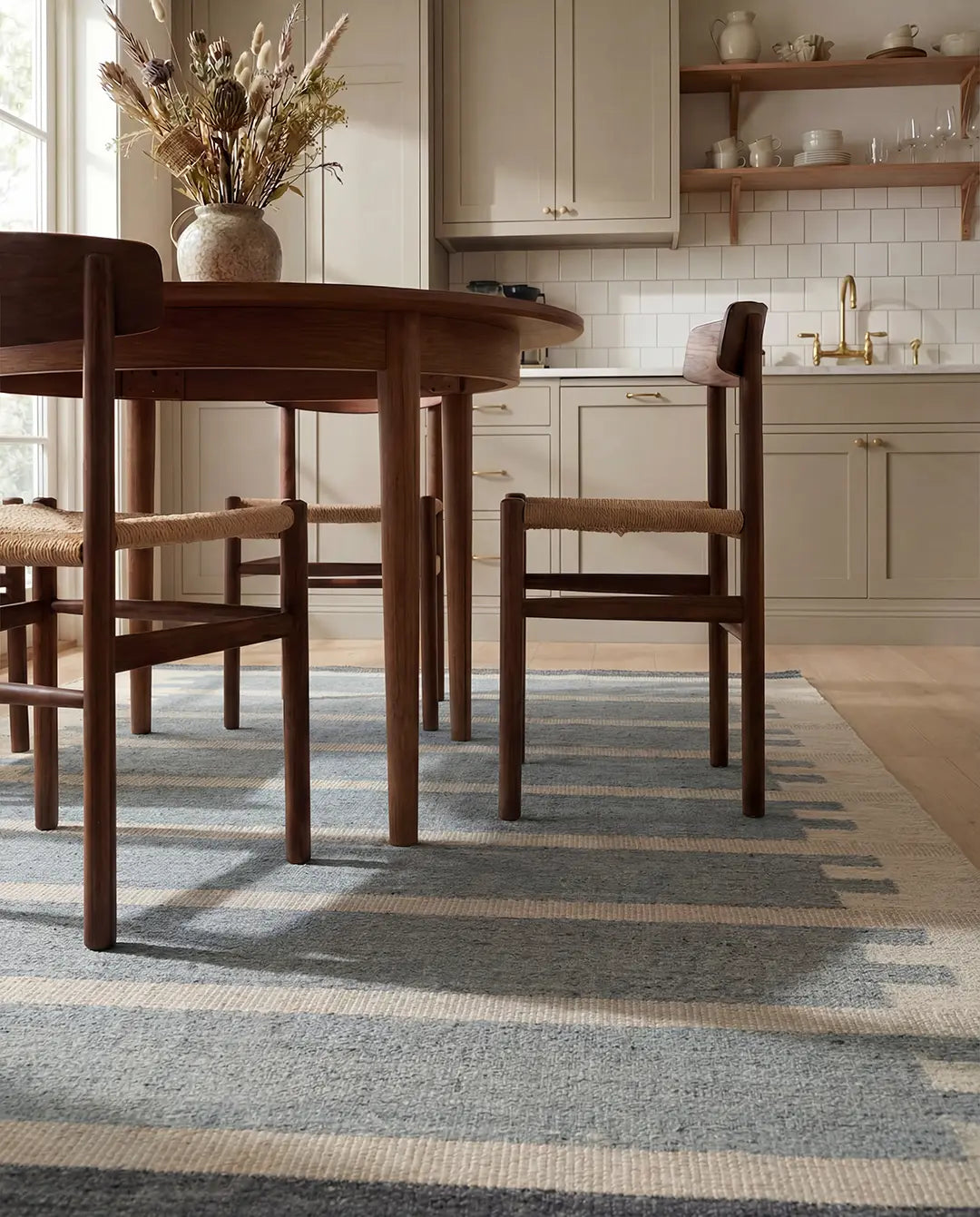 Randig matta i blått och beige under ett runt matbord i trä med stolar i en stilren köksmiljö.