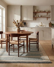 Runt matbord i mörkt trä med matchande stolar och en mönstrad matta i ett ljust, modernt kök.