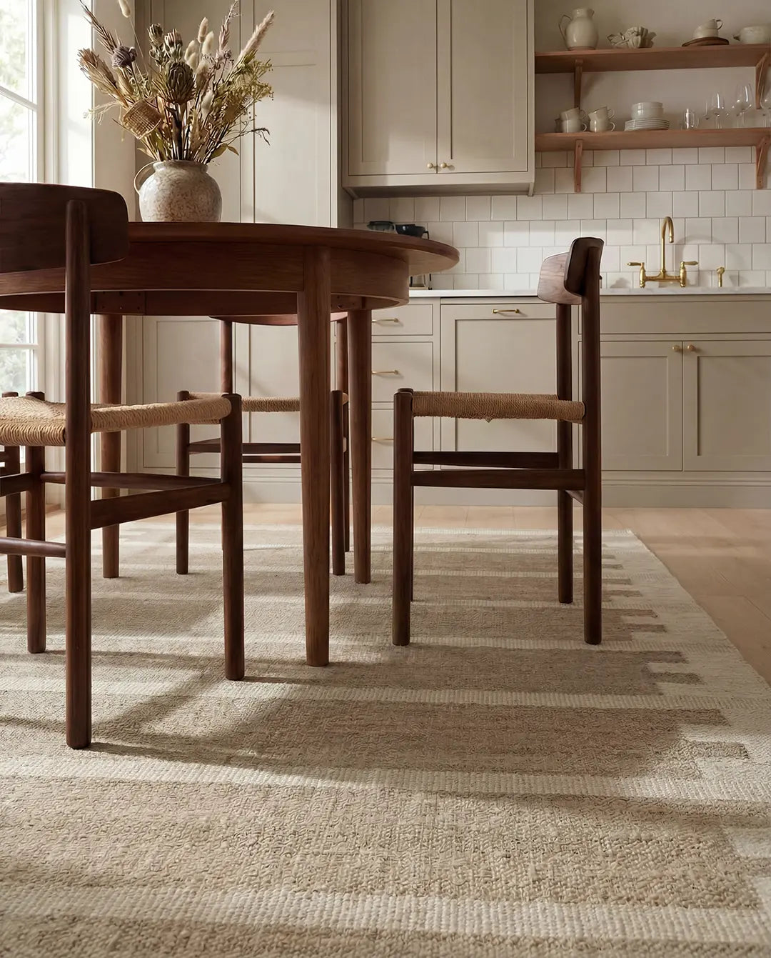 Beige matta med geometriskt randigt mönster under ett runt matbord i mörkt trä med stolar i modern skandinavisk design.