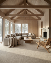 Modern beige sectional sofa in a wood-paneled living room with a stone fireplace, live-edge coffee table, and snowy view.