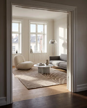 Handtuftad ullmatta Zebra Beige från Classic Collection med zebramönster i beige och off-white, fotograferad i ett ljust vardagsrum med soffa, fåtölj och marmorbord.