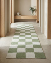 Moderner Flurläufer mit kariertem Schachbrettmuster in Salbeigrün und Creme auf hellen Fliesen.