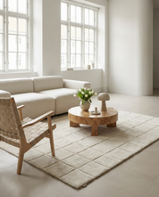 Modern living room with a burl wood coffee table, cream modular sofa, woven wooden chair, and a textured grid-pattern rug.
