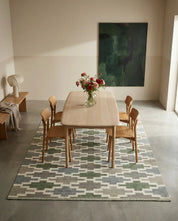 Light wood dining table and four matching chairs set on a green and grey geometric patterned area rug.