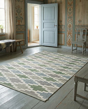 Rectangular area rug with a geometric green, blue, and gray pattern, centered in a rustic room with wood floors.