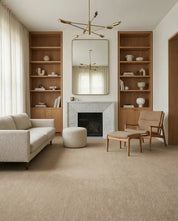 Modern living room with beige sofa, accent chair, ottoman, marble fireplace, and tall wooden bookshelves.