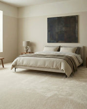 Minimalist bedroom featuring a low-profile beige upholstered bed with neutral linen bedding and a soft textured carpet.