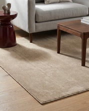 Handvävd ullmatta Lodge i färgen Natural Beige från Classic Collection, placerad i ett vardagsrum med soffa och soffbord i trä. Den mjukt melerade luggen ger mattan ett levande och taktilt uttryck.