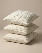 Stack of three square cream-colored throw pillows with textured, tufted patterns on a beige background.