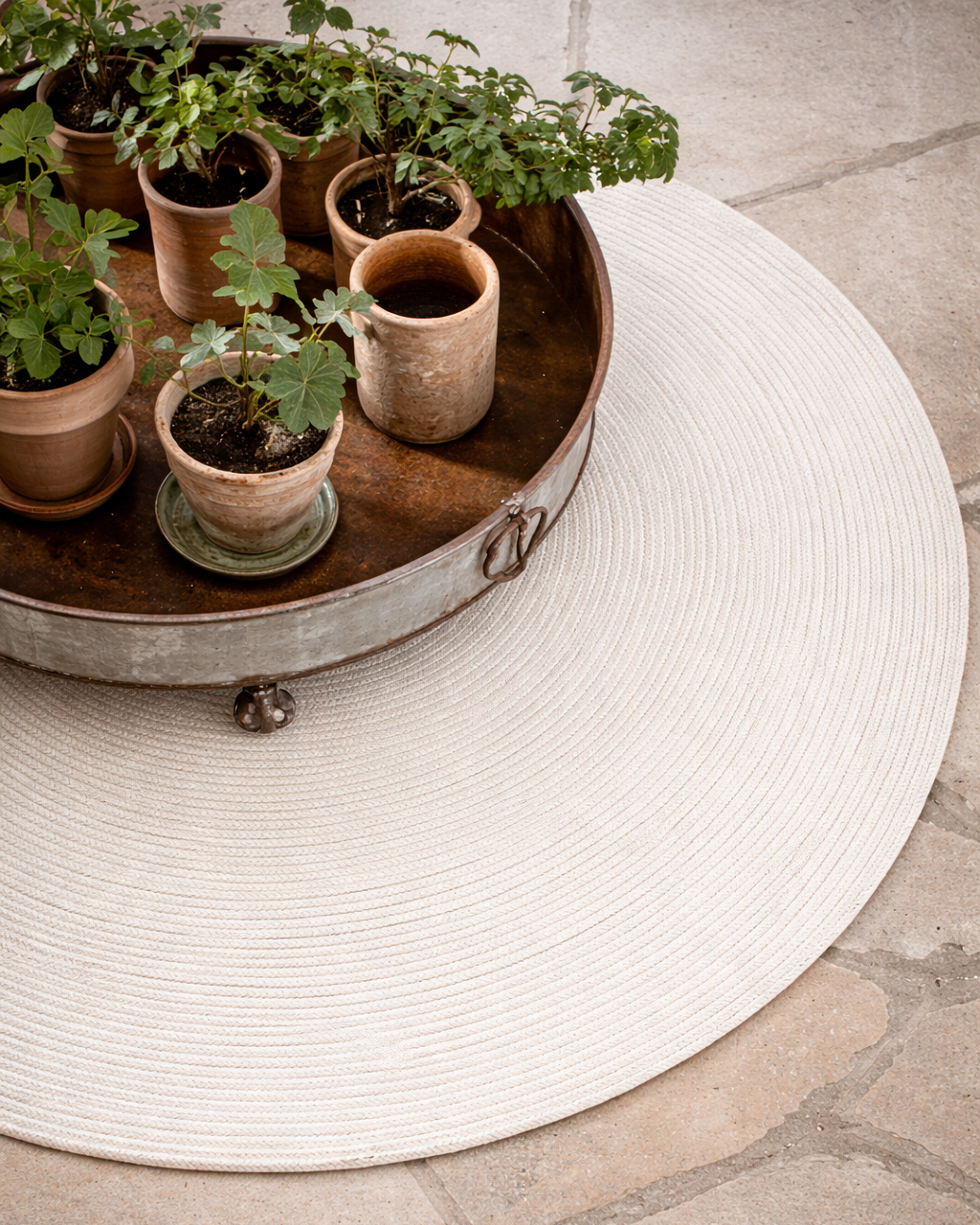 Miljöbild, detalj med möbel
Vit rund ullmatta Merino i ull med cirkulär struktur, delvis täckt av lågt bord med krukväxter