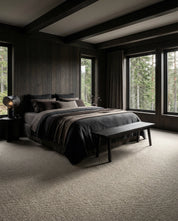 Luxuriöses Schlafzimmer mit dunkelgrauer Bettwäsche, Holzvertäfelung und hellem strukturiertem Teppichboden.