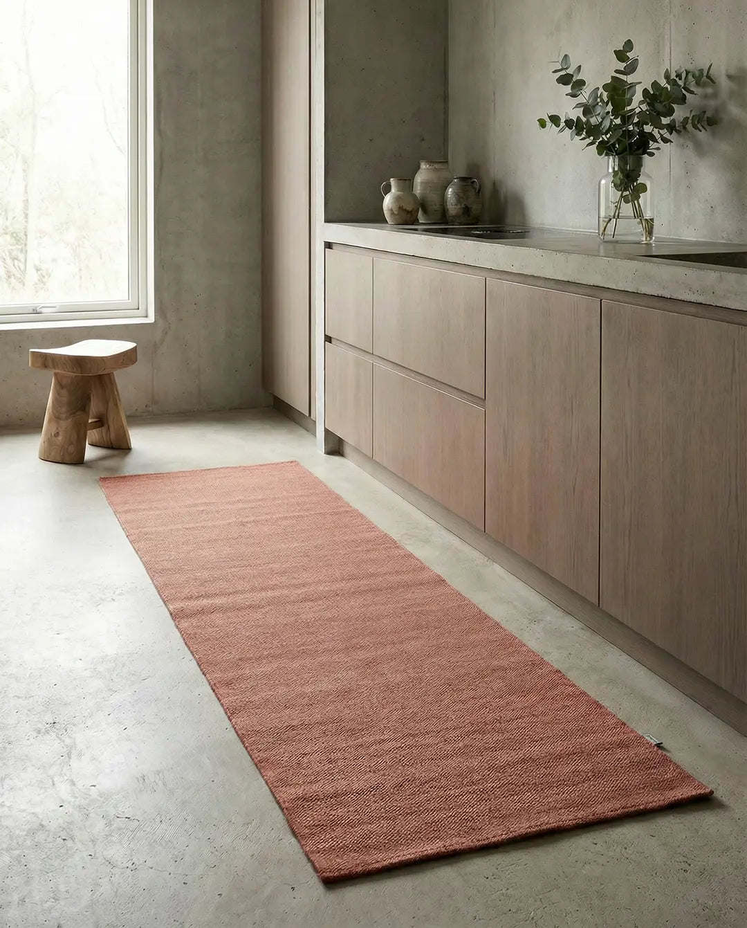 Lång, rektangulär matta i dämpad terrakotta med subtil vävd struktur på ett betonggolv i ett modernt kök.