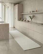 Long beige woven runner rug placed on a polished concrete floor in a modern minimalist kitchen.