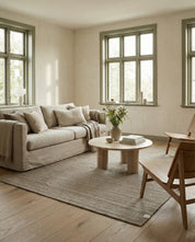 Beiges Wohnzimmer mit beigem Leinen-Sofa, runden Holztisch, Stühlen und einem grauen Teppich in natürlicher Einrichtung.