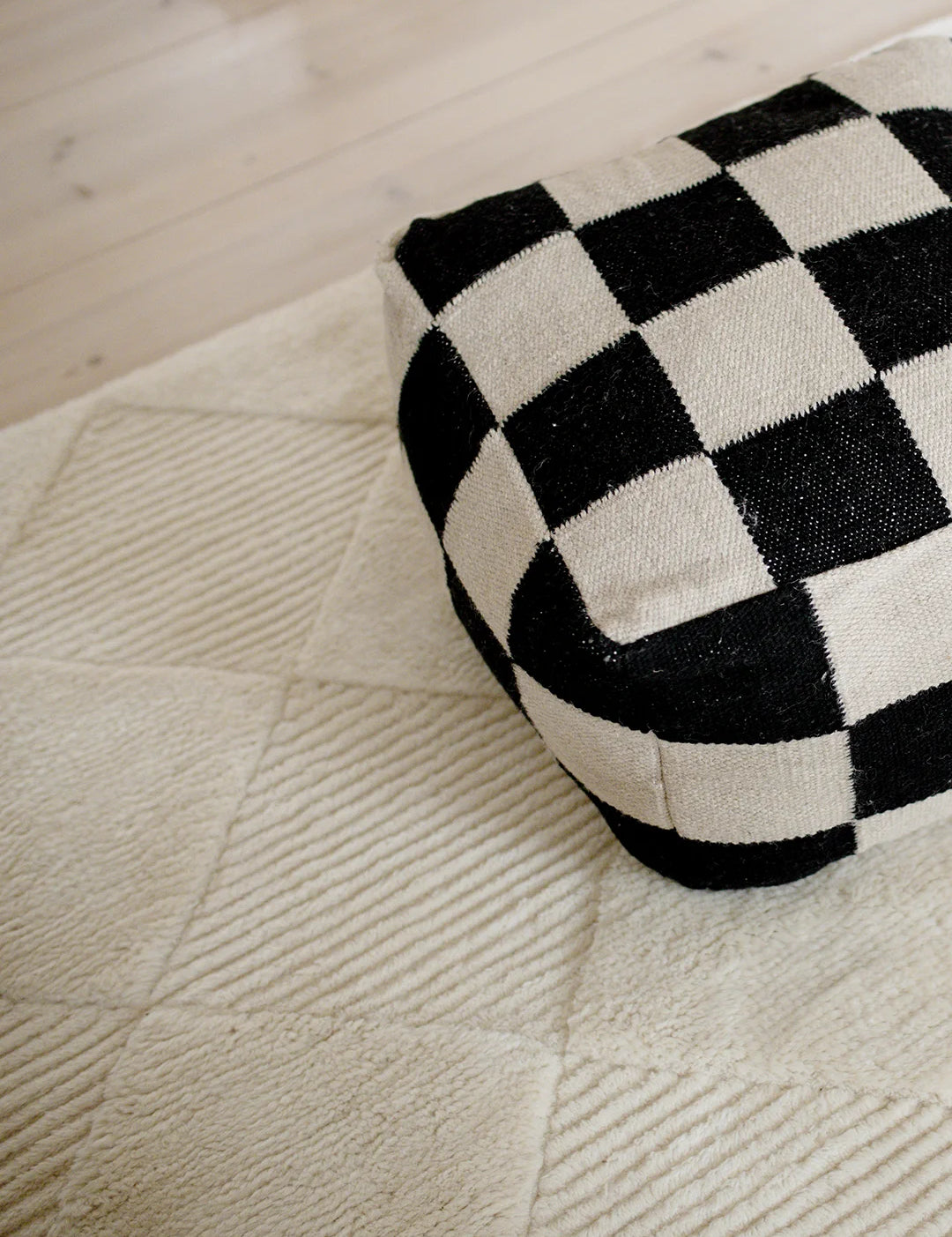 Natur, 50x50 cm, handvävd i ull, placerad på en ljus strukturerad ullmatta.