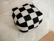 Puff Square Svart/Natur, 50x50 cm, handvävd i ull, placerad på en ljus strukturerad ullmatta.