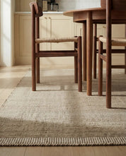 Beige vävd matta med texturerad yta placerad under en matgrupp i mörkt trä i en ljus matsal.