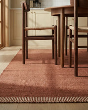 Textured terracotta area rug with a cream striped border under a wooden dining set in a modern kitchen.