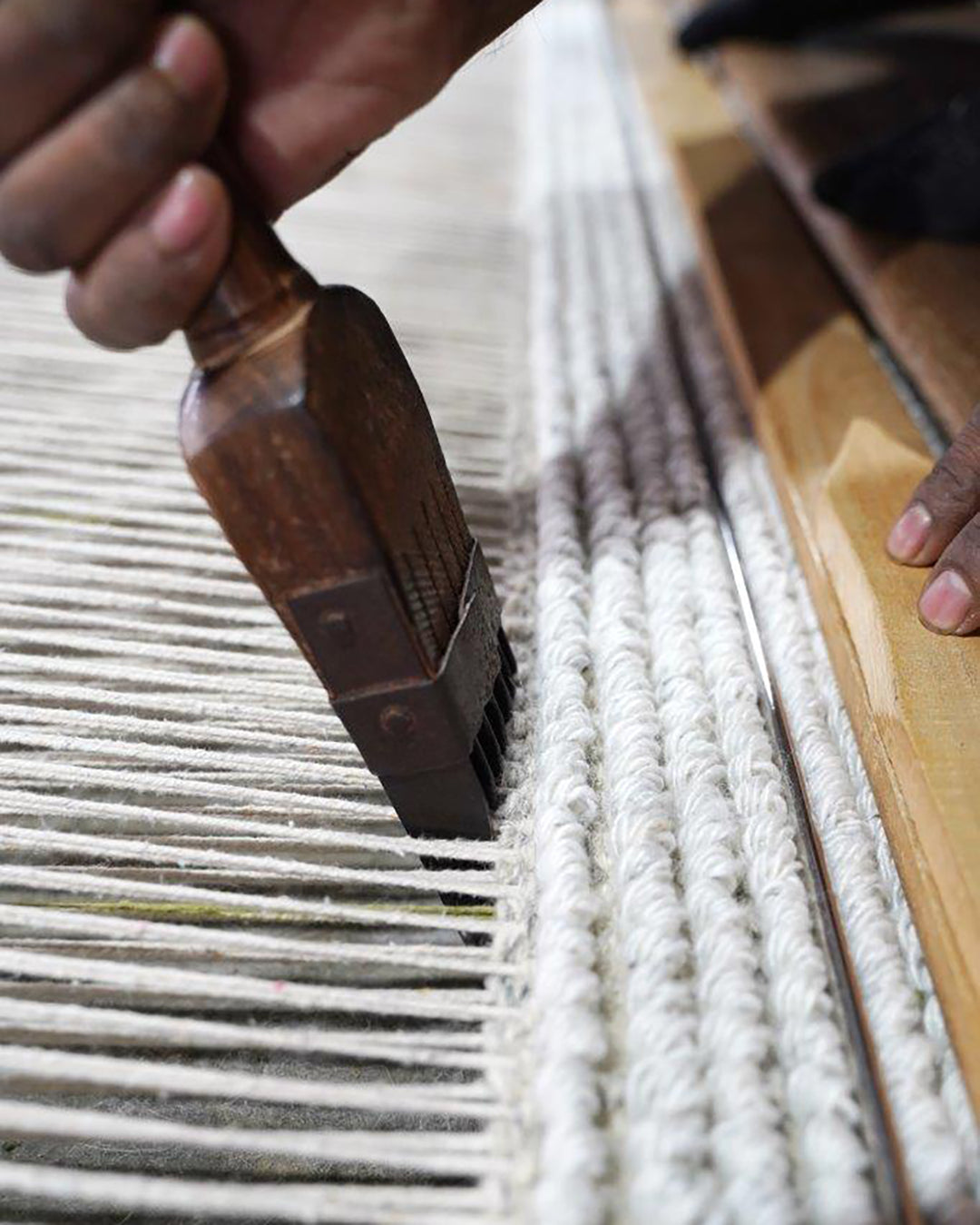 Närbild från mattproduktion i Indien där ullgarn bearbetas för hand i vävstol under tillverkningen av Classic Collections handgjorda mattor.