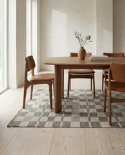 Modern dining set with oval wooden table and tan leather chairs on a grey and beige checkered area rug.