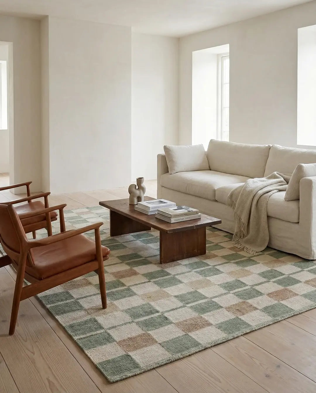 Wohnzimmer mit beigem Leinensofa, braunen Ledersesseln und einem karierten Teppich in Grün und Beige auf Holzboden.