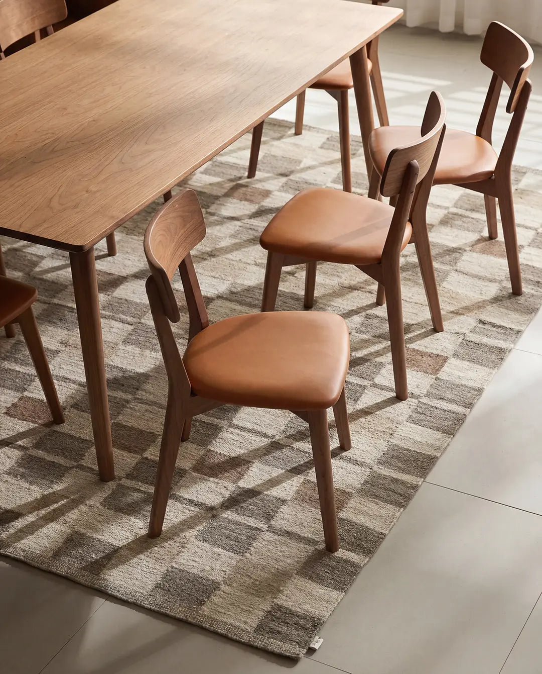 Esszimmerset mit Massivholztisch und Stühlen mit braunem Kunstlederbezug auf einem karierten Teppich.