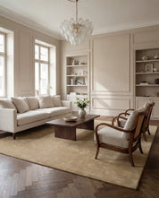 Beige living room featuring a modern sofa, wooden coffee table, and two vintage-style cane chairs on a textured rug.
