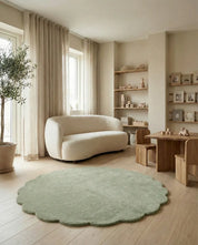 Round sage green scalloped area rug in a neutral modern nursery with cream bouclé sofa and wooden furniture.