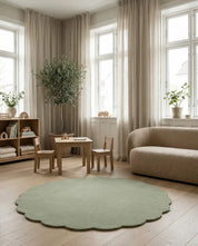 Scalloped sage green round area rug in a modern Scandinavian living room with wooden furniture and neutral decor.