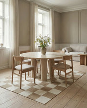 Runder Esstisch aus hellem Stein mit Säulenfuß und vier passenden Holzstühlen in einem modernen, beigen Wohnzimmer.