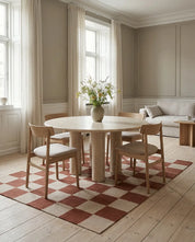 Runder Esstisch aus hellem Naturstein mit Säulenbeinen, umgeben von modernen Holzstühlen auf einem karierten Teppich.