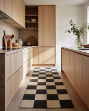 Moderner Küchenläufer mit schwarz-weißem Schachbrettmuster zwischen hellen Holzschränken.