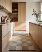 Moderner Küchenläufer mit grau-beigem Schachbrettmuster auf hellem Holzboden zwischen minimalistischen Küchenfronten.